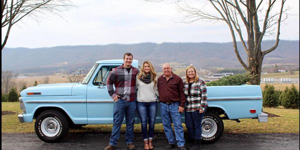 Family of four standing beside a vintage blue pickup truck outdoors.