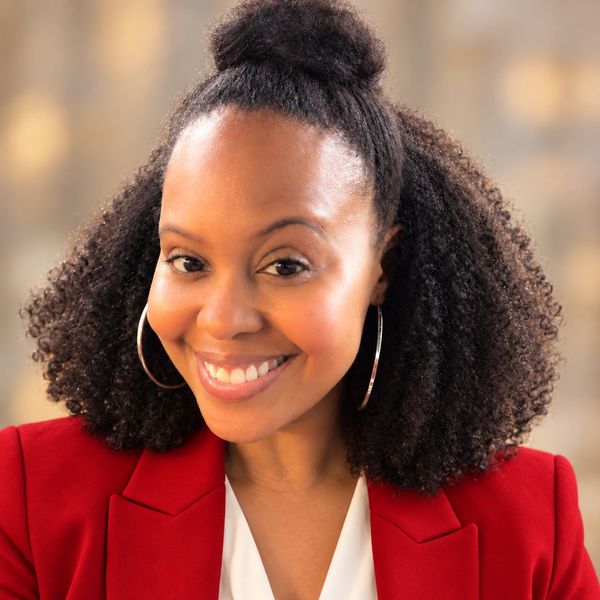 Smiling woman with curly hair wearing red blazer.