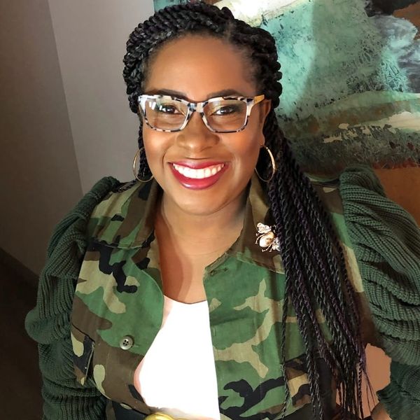Smiling woman with braided hair and camouflage jacket.