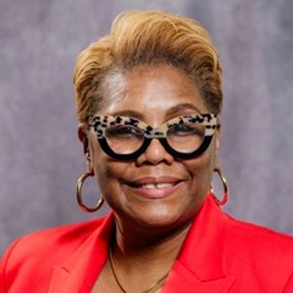 Smiling woman with stylish glasses and red blazer.