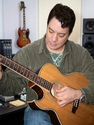 Man playing an acoustic guitar in a music studio.