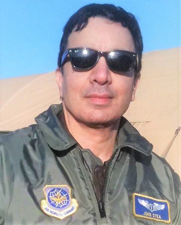 Man wearing aviator sunglasses and military flight jacket outdoors.