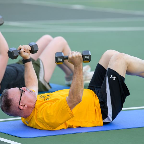 Two people exercising with dumbbells on mats outdoors.