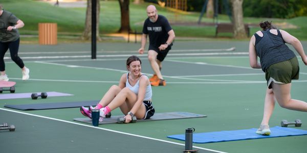 People exercising outdoors on fitness mats with dumbbells on a basketball court.
