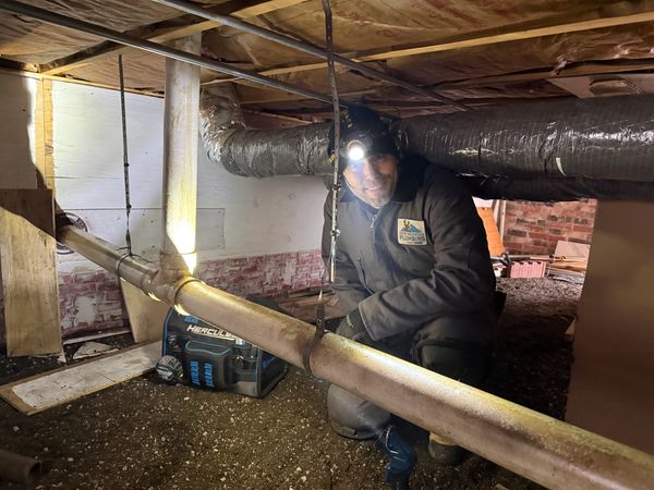 Worker inspecting pipes in a crawl space with a headlamp.