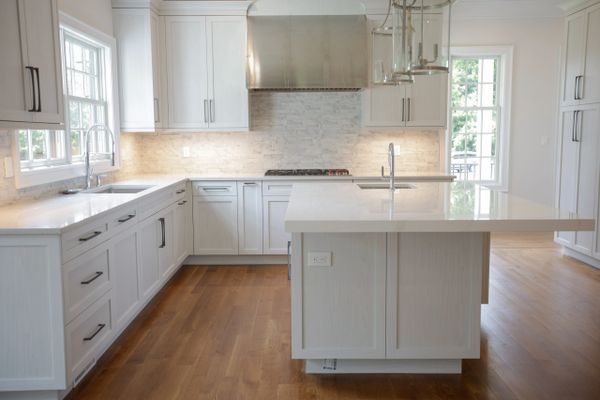 Modern white kitchen with marble countertops and wooden floors.