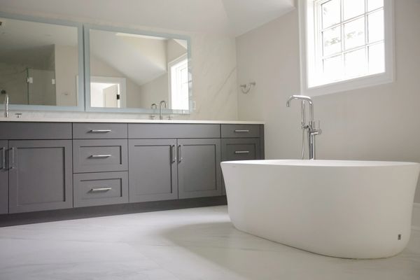 Modern bathroom with gray cabinetry and a freestanding white bathtub.