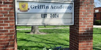 Sign for Griffin Academy established in 2024, set between brick pillars with spring greenery.