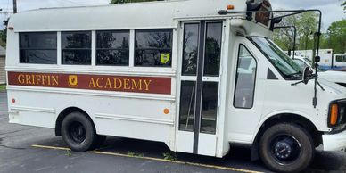 White school bus with Griffin Academy logo and name parked on asphalt.