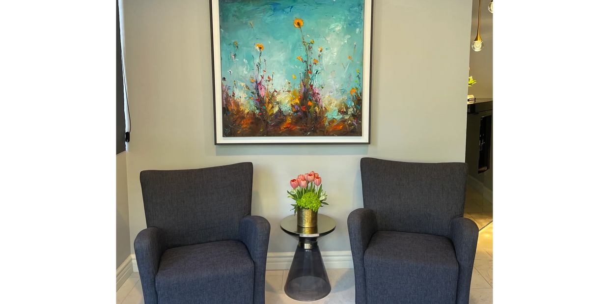 Two gray armchairs with a side table and floral painting.