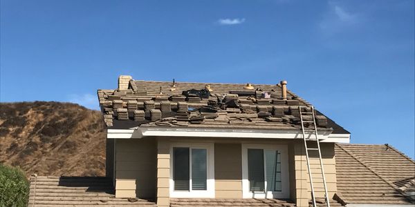 Roof repair in progress with workers and ladders on a sunny day.