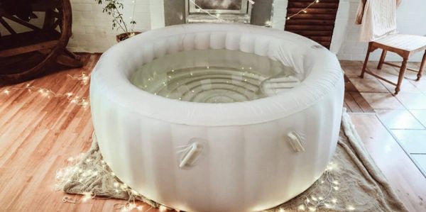 Inflatable white tub filled with water, placed indoors on a rug with string lights around.