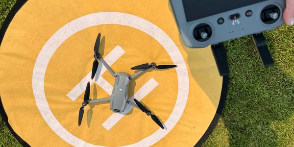 Drone on a yellow landing pad with remote controller in hand.