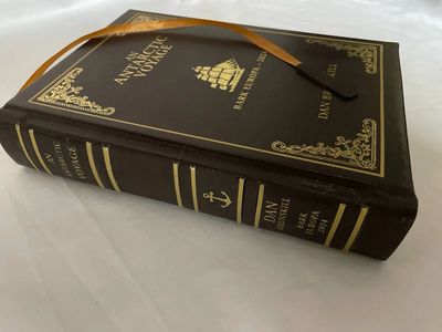 A leather-bound book titled 'The Anzac Voyage' by Dan Marshall with a golden ribbon bookmark.
