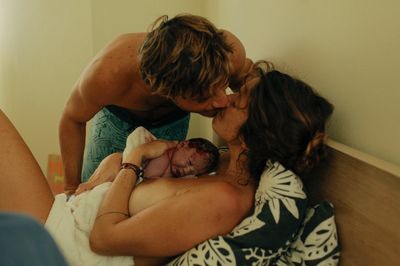 Home birth mom holding her newborn baby in bed kissing her partner