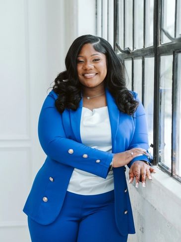 Confident woman in a blue suit smiling by a window.