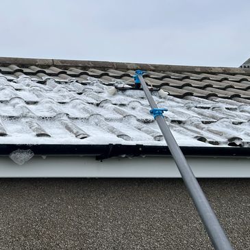 Long pole brush cleaning foam off roof tiles.