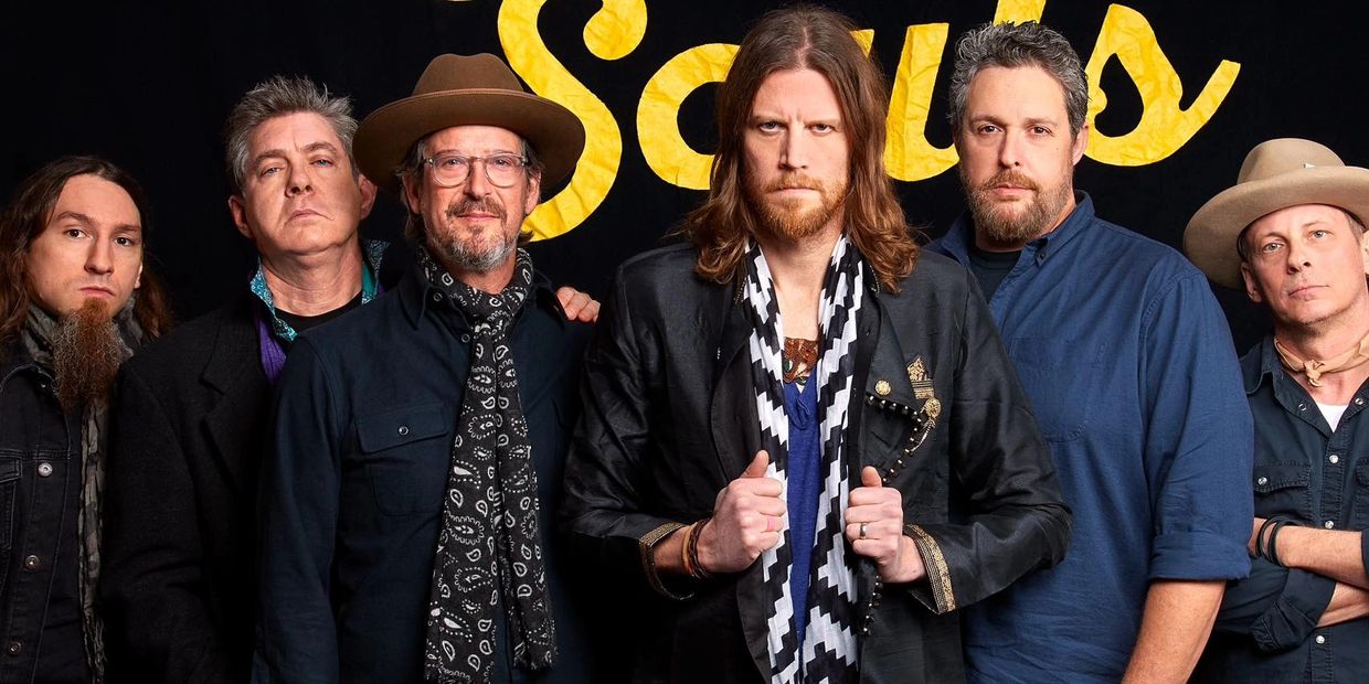 A group of six men posing together in front of a black background with yellow text.