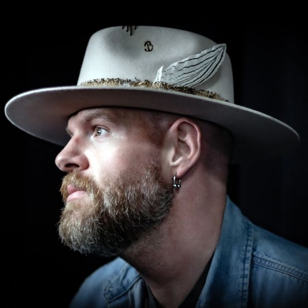 Bearded man wearing a decorated hat and hoop earrings.