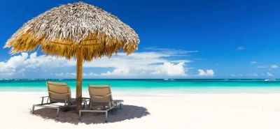 Two lounge chairs under a thatched umbrella on a sunny beach.