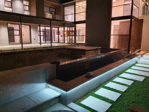 Modern backyard at night with illuminated pool and stepping stone pathway.