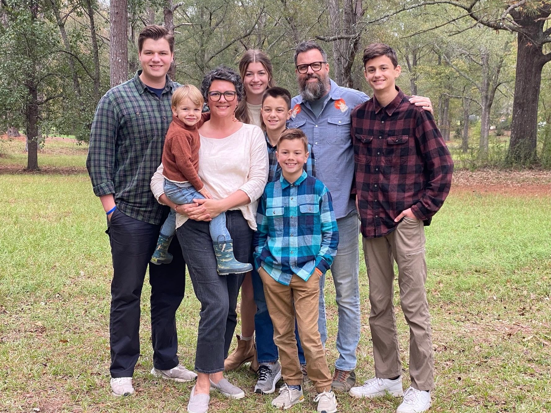 Family picture standing outside on grass with trees in the background