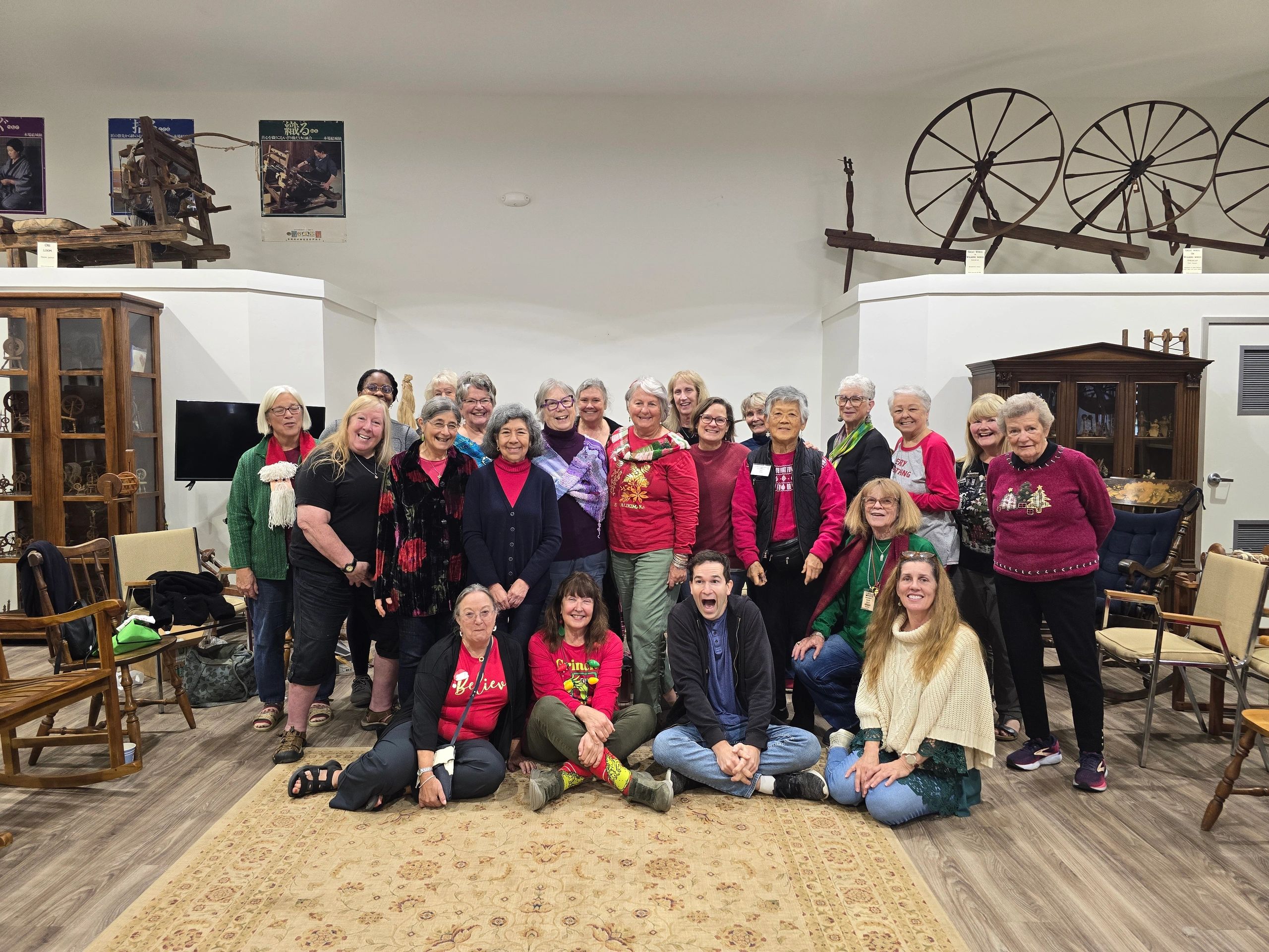 Group photo of smiling adults in a room with wooden furniture and spinning wheels.