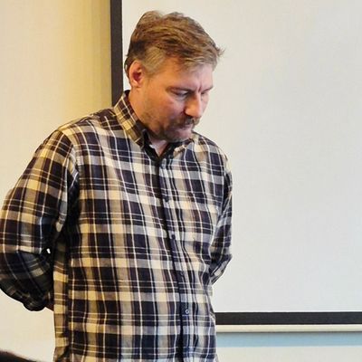 Man in plaid shirt looking down thoughtfully.