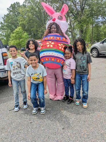 Children standing with pers dressed as large bunny holding an Easter Egg