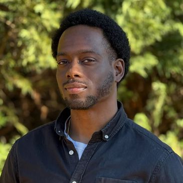 Man with a confident expression wearing a black shirt outdoors.