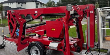 Red mobile lifting machine parked on paved driveway near houses.