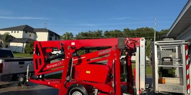 A red lift machine parked outdoors near buildings under a clear sky.