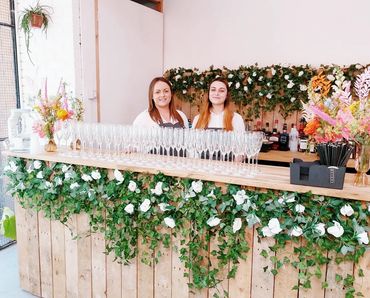 Pallet bar at wedding with faux white florals, serving prosecco arrival / welcome drinks