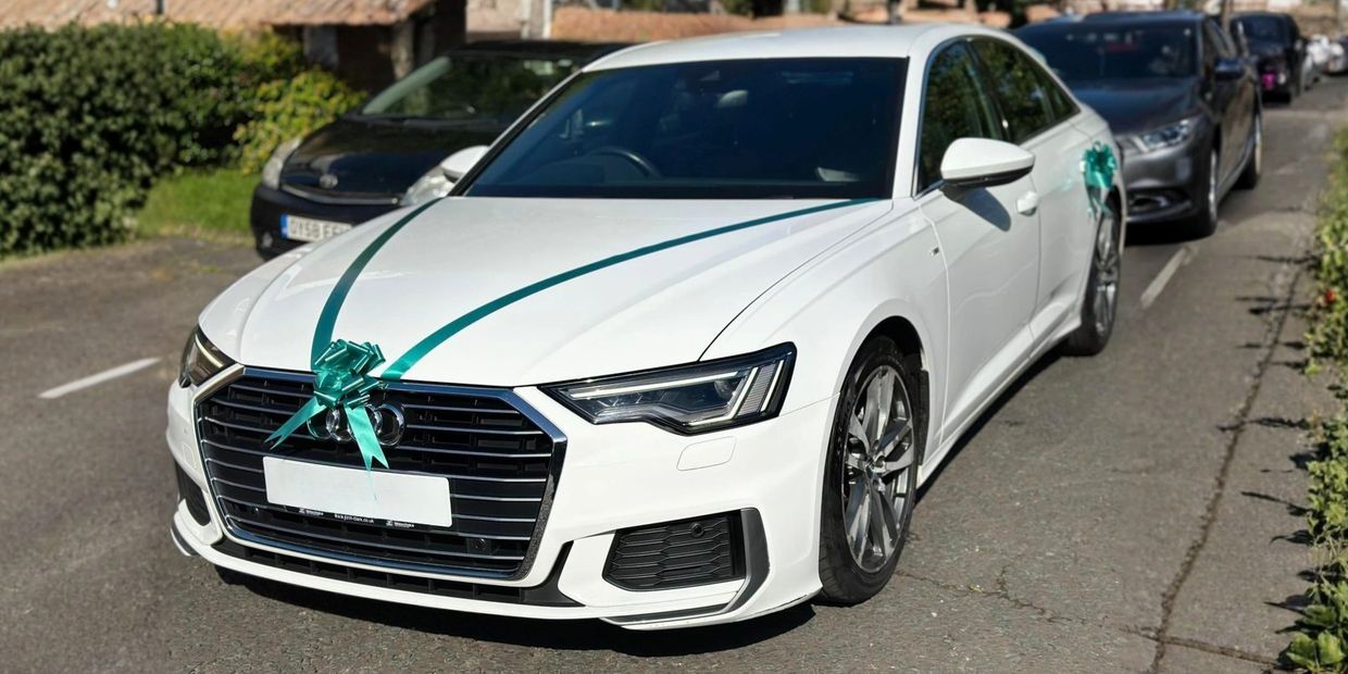 White Audi decorated with green ribbons on a road.