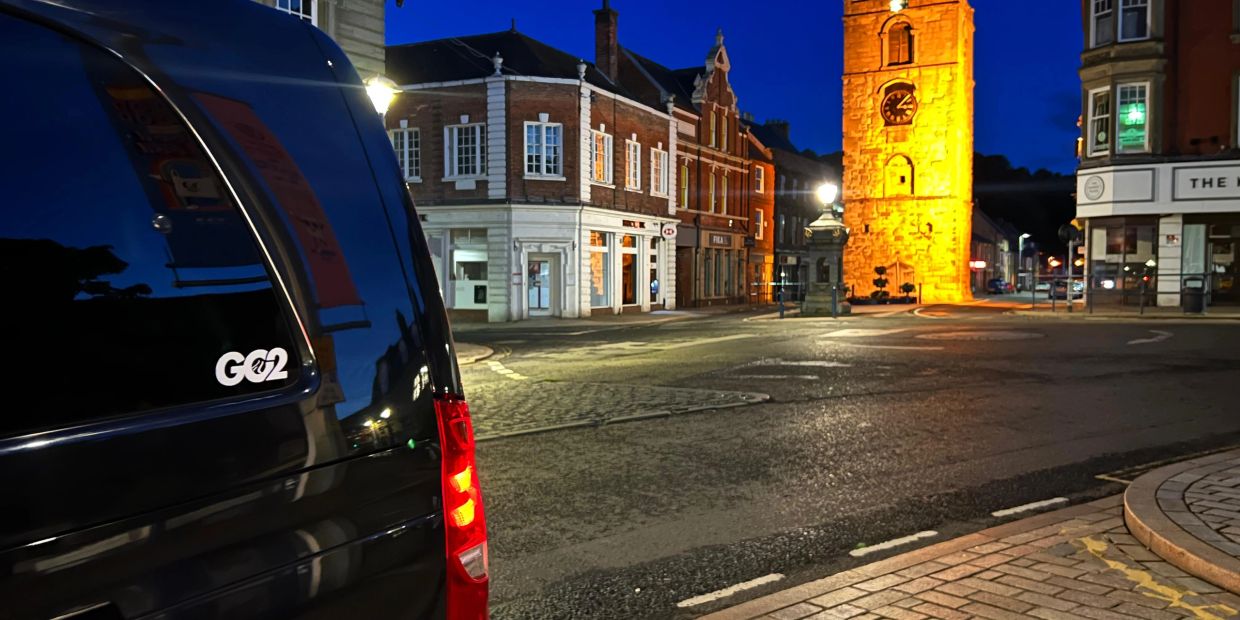 Nighttime street view with illuminated clock tower and parked black vehicle.