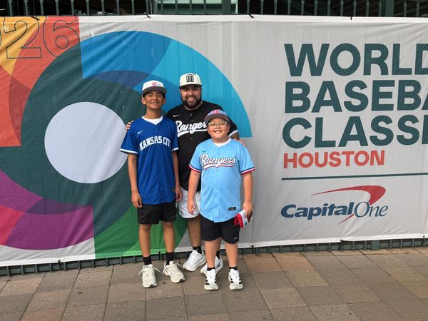 Three boys in baseball jerseys posing in front of a World Baseball Classic Houston banner.