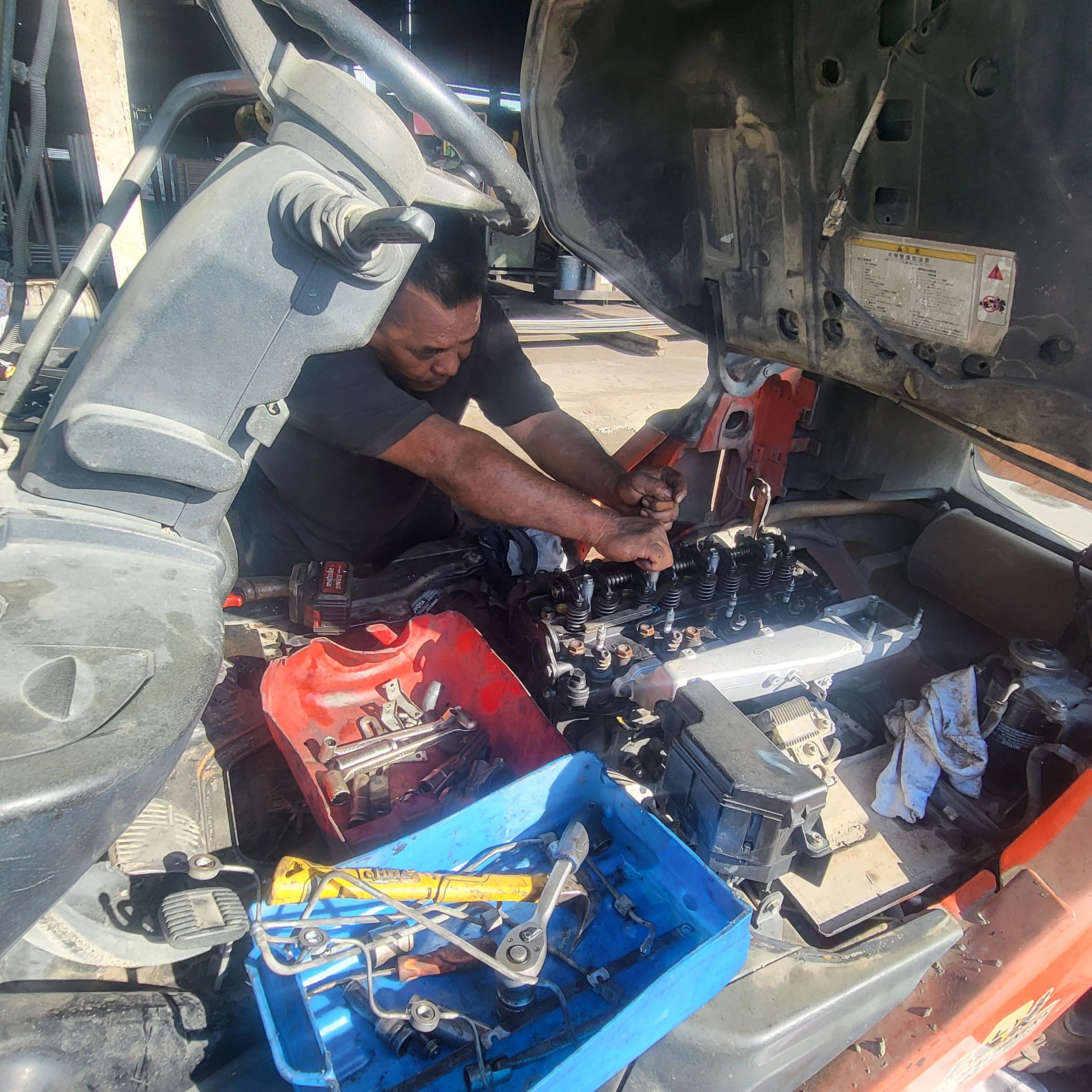 Man repairing vehicle engine with tools around.