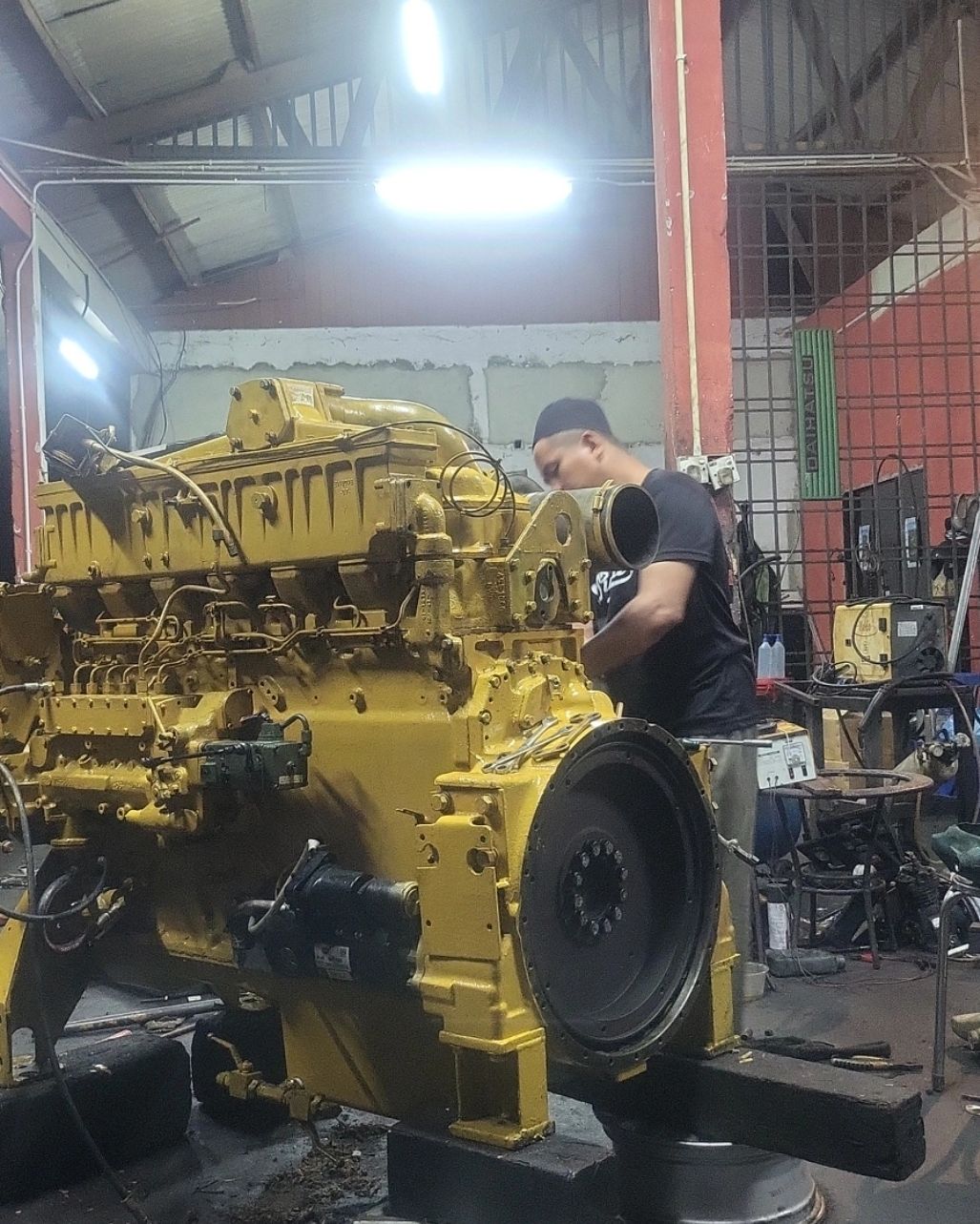 A man working on a large yellow engine in a workshop.
