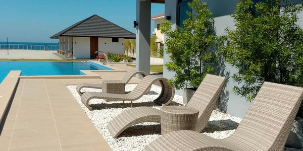 Modern poolside lounge chairs beside a sleek pool under clear blue skies.