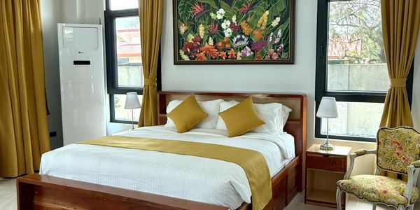Modern bedroom with wooden bed, mustard curtains, and floral painting.