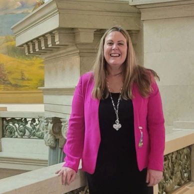 Smiling woman in pink blazer inside a historic building.