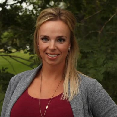 Smiling woman outdoors with blonde hair and casual attire.