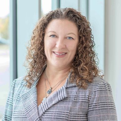 Smiling woman with curly hair in checked blazer.