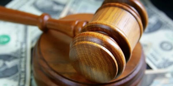 A wooden judge's gavel resting on a base with US dollar bills underneath.