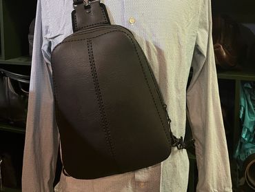 Black leather sling bag on a mannequin with a white shirt.