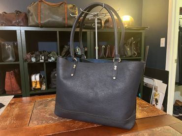 Black leather tote bag on a wooden table.