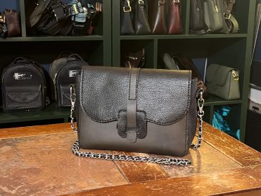 Black leather handbag with chain strap on a wooden table.