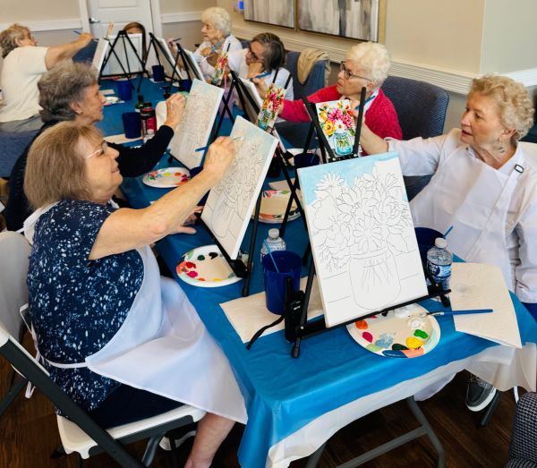 Elderly women painting flowers in a group setting.
