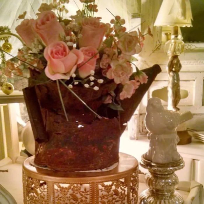 Rustic watering can used as a vase with pink flowers on a decorative golden stand.