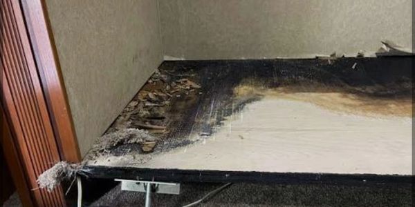 Burned and damaged wall with exposed wiring and damaged floor